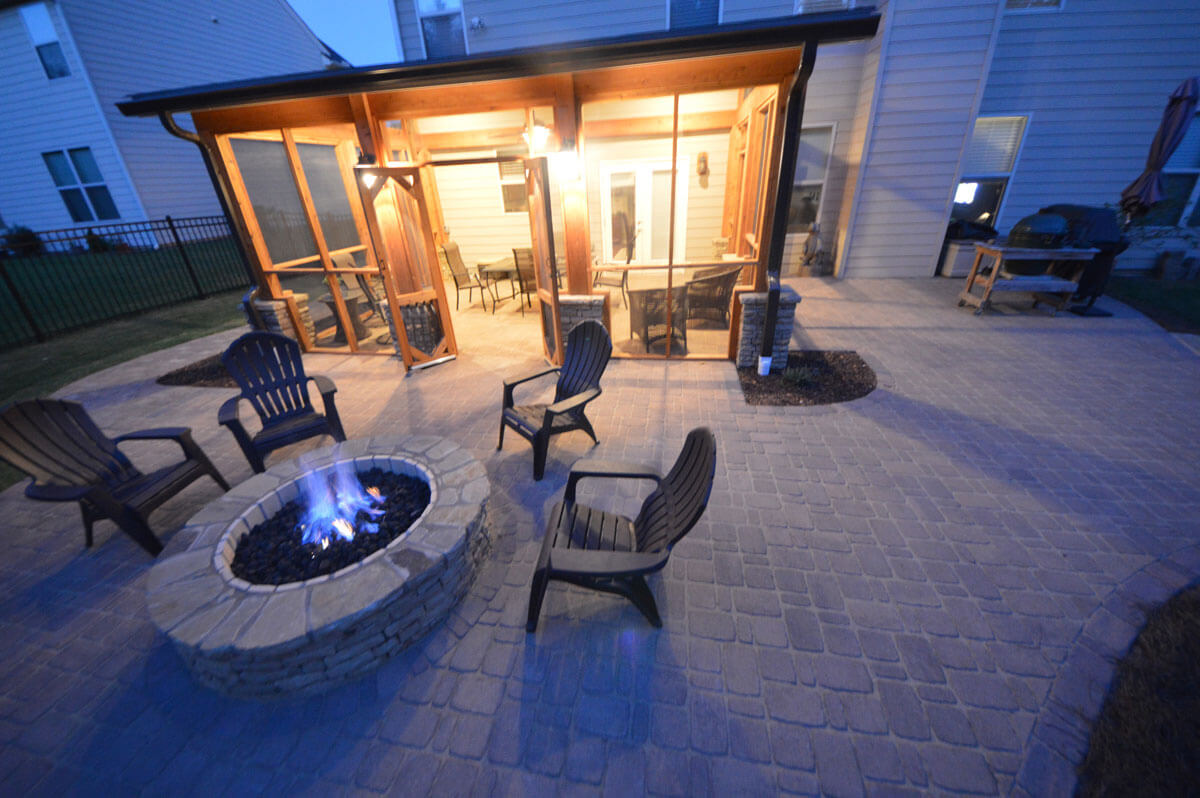 backyard outdoor chairs around stone fire pit and backyard screened-in porch