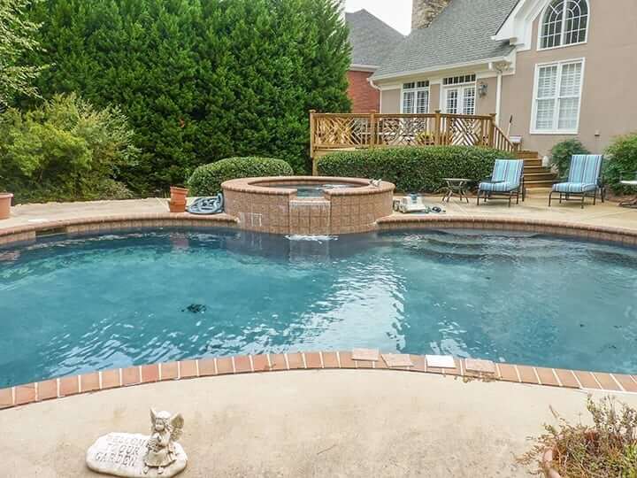 poolside view of pool with landscaping, brick hot tub and backyard wooden deck