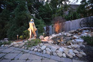 stonescaping and hardscaping with wooden fence and exterior lit statue