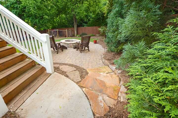 wooden and stone stairways leading down to backyard patio with chairs and stone fire pit