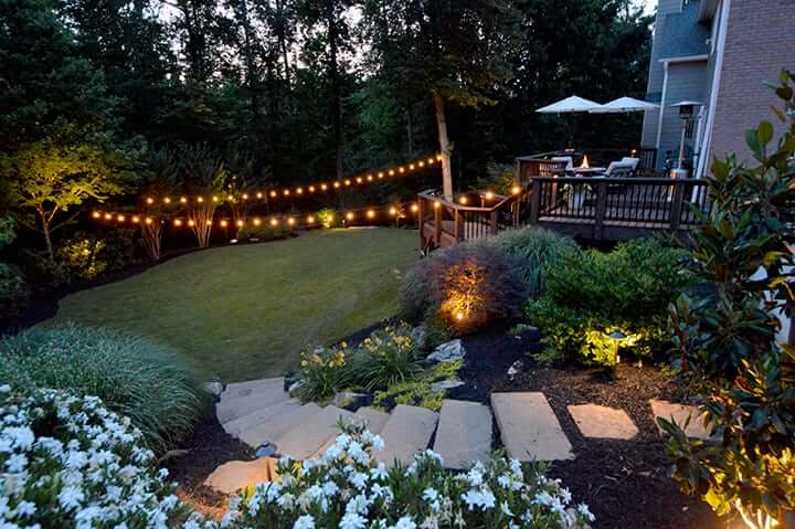 backyard with stone landscape stairs leading to grass living space with outdoor hanging string lights
