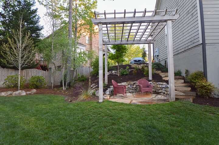 outdoor pergola structure with stone stairway in backyard with green grass and trees