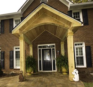 wooded portico on front of brick house with a black door and stone walkway