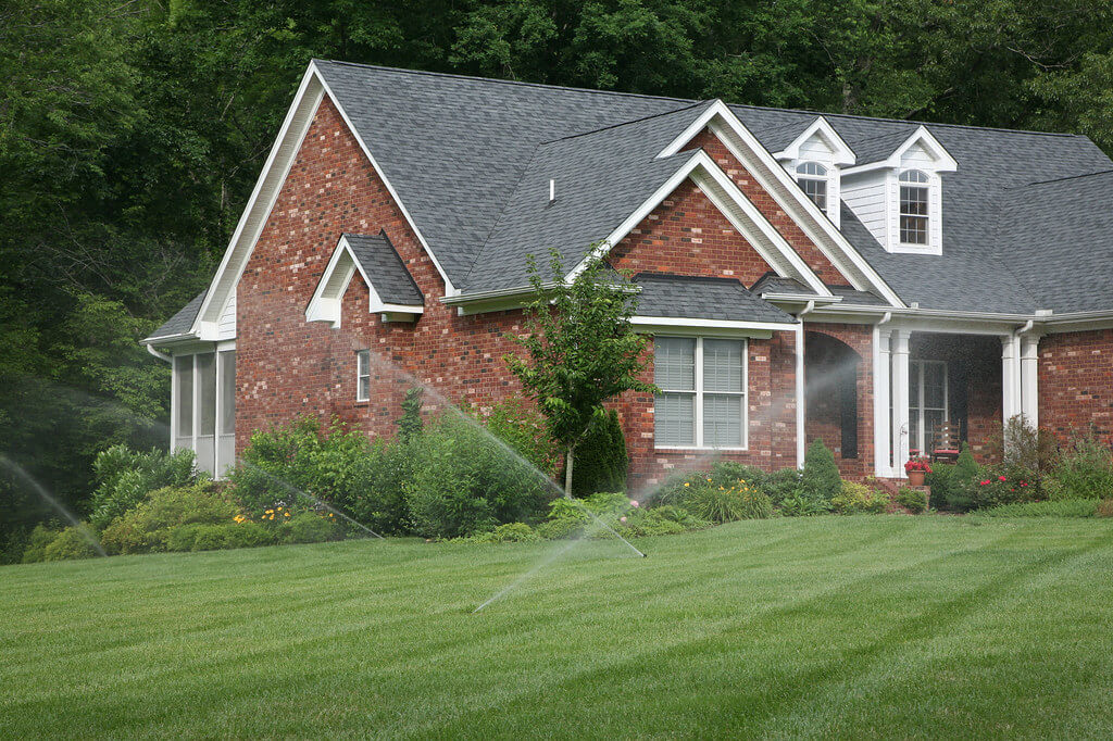 criss-crossing spraying lawn sprinkler irrigation system on grass yard of brick house