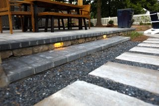 Small lights are set into broad stone steps beside a garden walkway of pale rectangular slabs separated by gravel.
