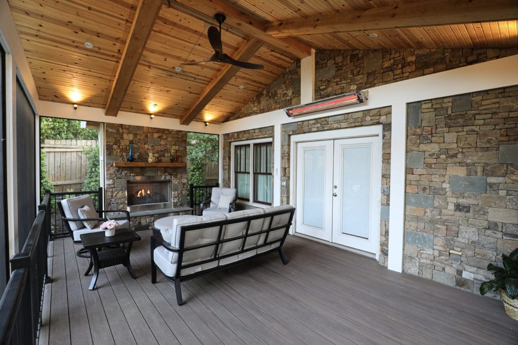 Screened porch with a wood ceiling, ceiling fan, stone fireplace, cushioned seating, table, French doors to the interior, and an overhead heater.