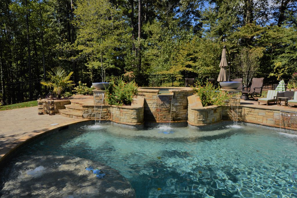 Water flows from stone spillways into a curved pool beside raised planting areas and a broad patio.